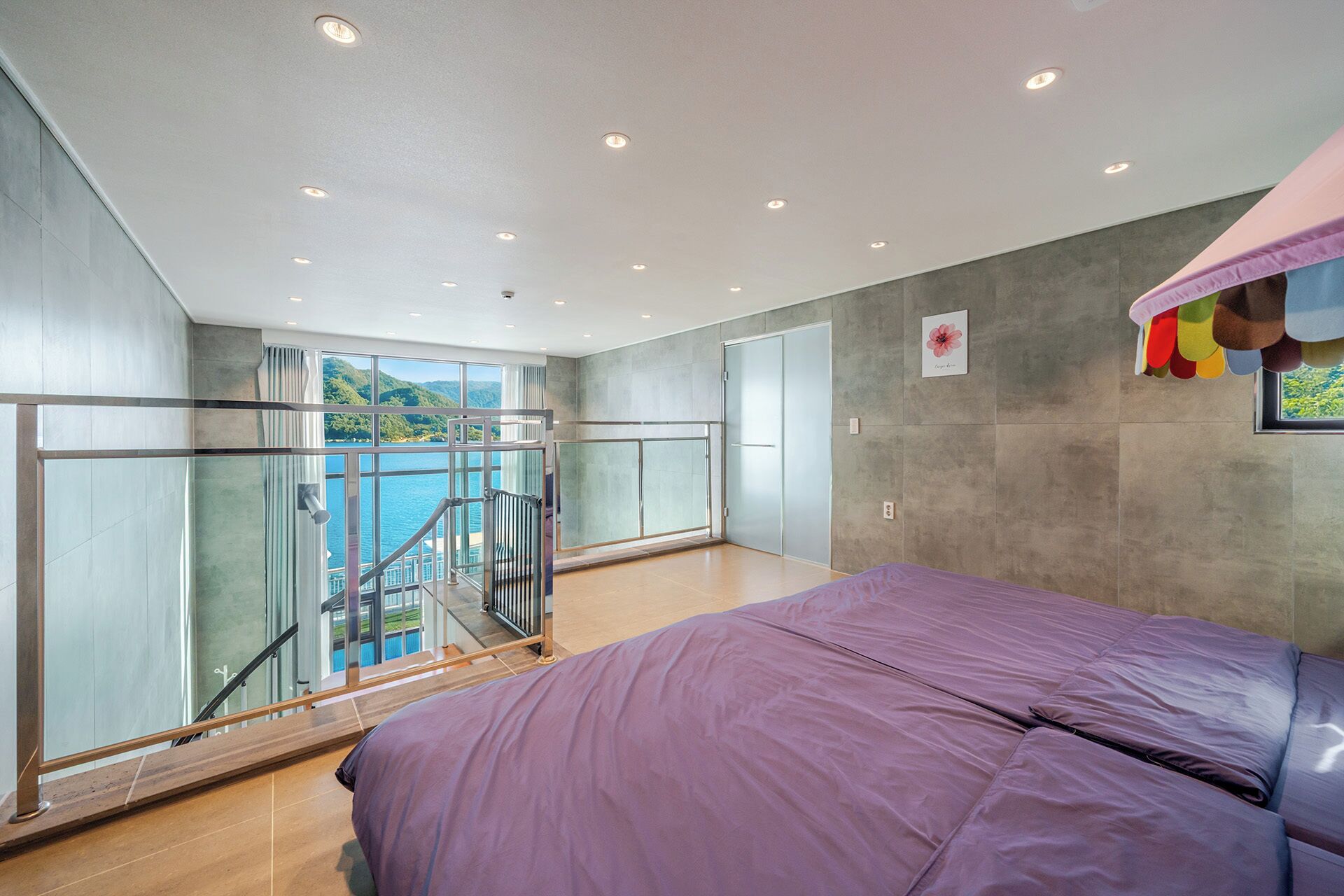 A bedroom with a large bed, a balcony with a glass door, and a view of a body of water.