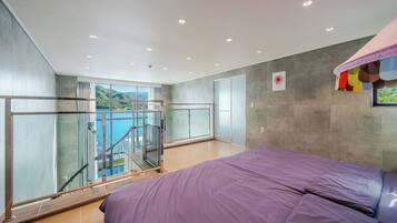 A bedroom with a large bed, a balcony with a glass door, and a view of a body of water.