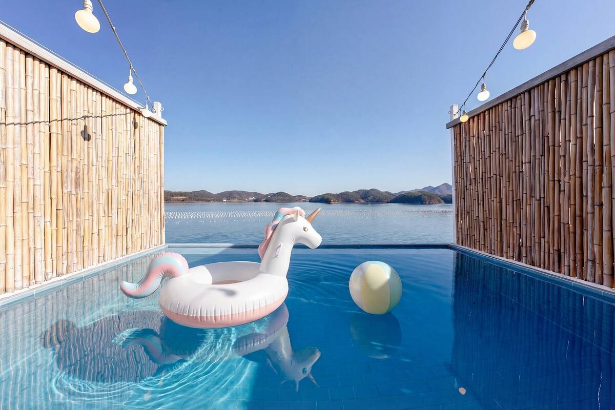Una piscina con un flotador de unicornio, paredes de bambú y una vista despejada del lago.