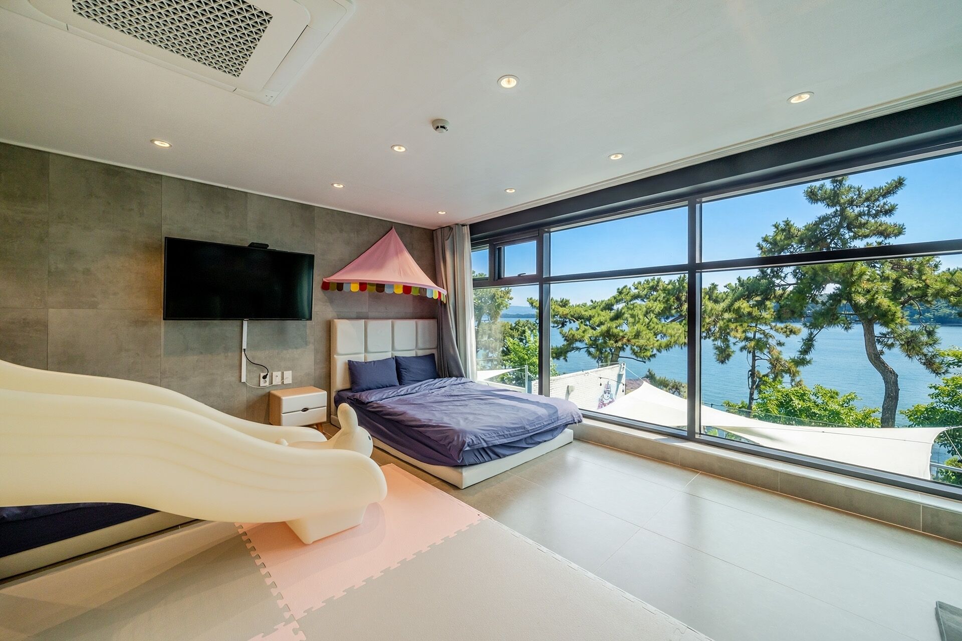 A modern bedroom with a bed, a TV, and a large window overlooking a lake.