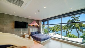 Un dormitori modern amb un llit, un televisor i una finestra gran amb vista a un llac.