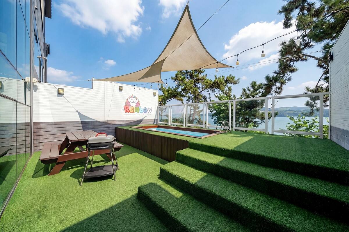Un patio trasero con piscina, césped artificial, una parrilla y vistas a un lago.