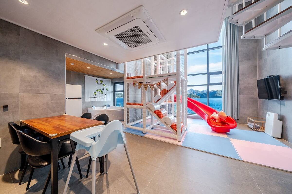 Un interior moderno con comedor, zona de juegos con tobogán y un amplio ventanal con vistas.