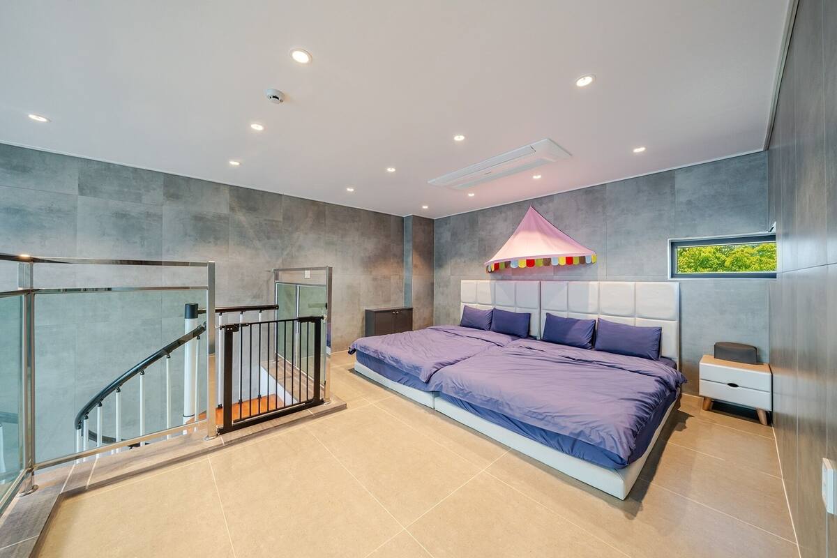 Un dormitorio moderno con una cama grande, una escalera con cerramiento de vidrio y vistas al exterior.