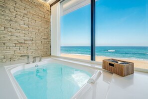 Ein Badezimmer mit Steinwand, einer Badewanne und Blick auf den Strand.