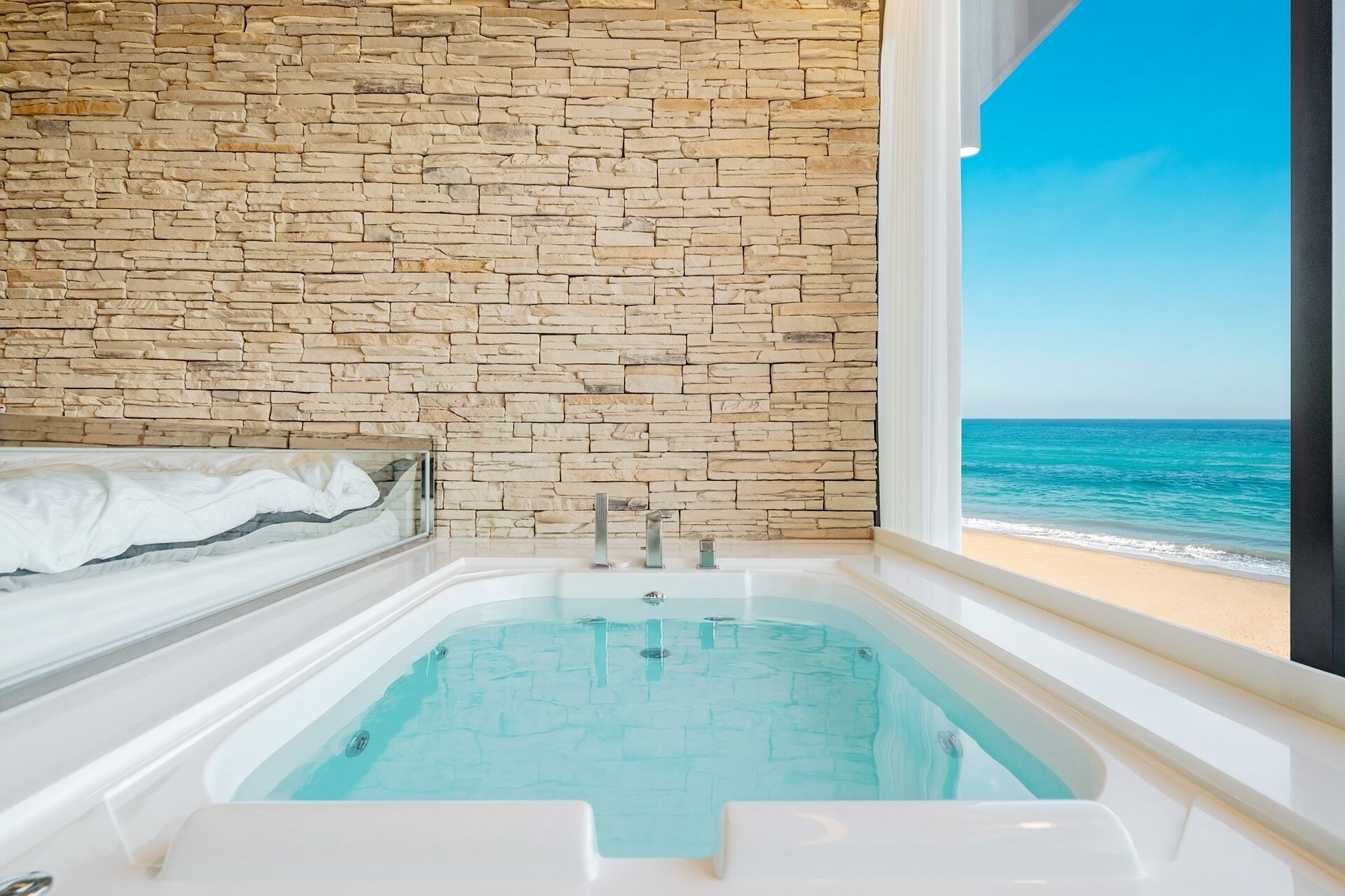 A bathroom with a stone wall, a bathtub, and a view of the ocean.