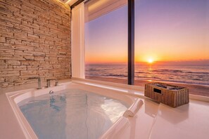 Un bagno con parete in pietra, una vasca da bagno e vista sul tramonto sull'oceano.