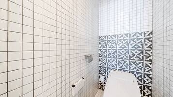 A bathroom with white tiled walls, a patterned tile accent wall, a toilet, and a towel rack.