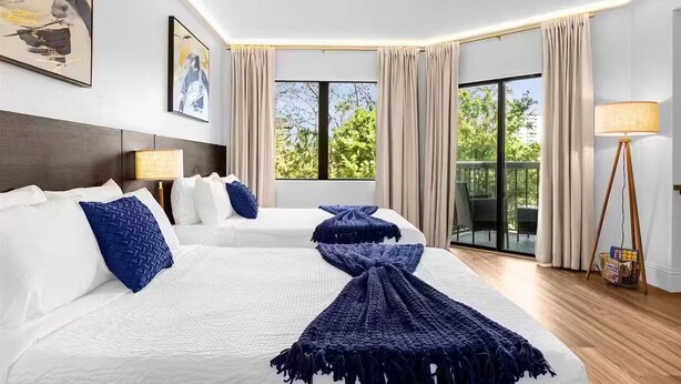 Une chambre d’hôtel avec un grand lit, deux tables de chevet, une lampe sur pied et une vue sur la verdure.