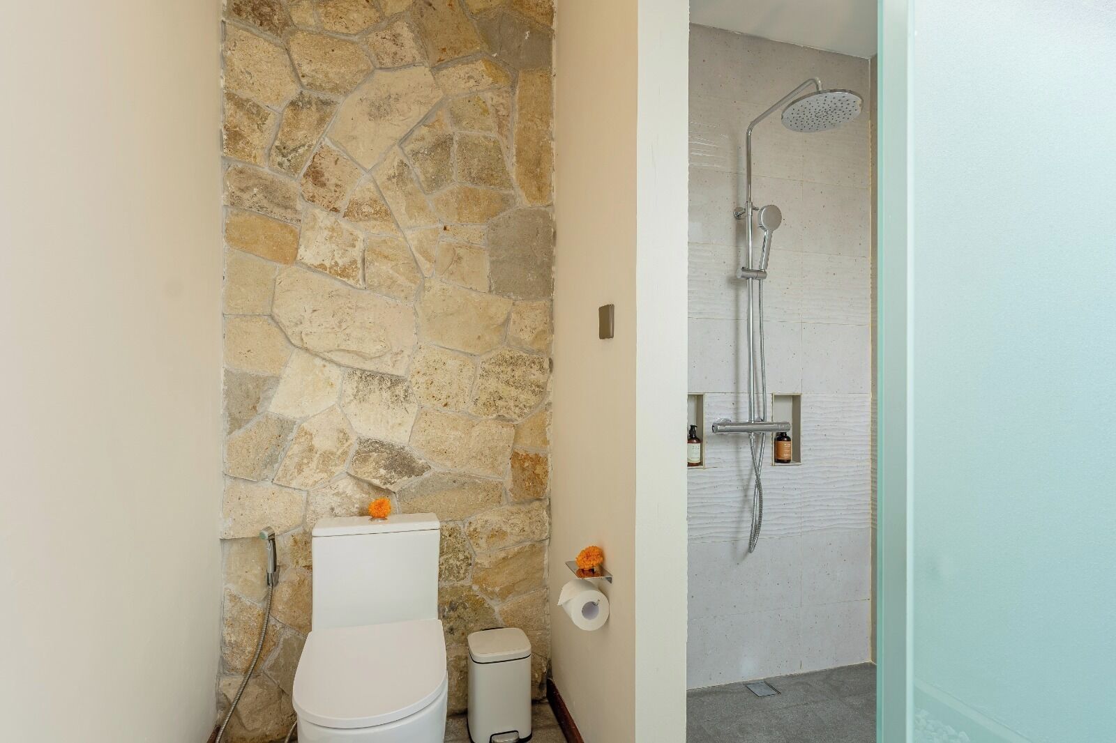 A bathroom with a stone wall, a toilet, a bidet, and a shower.