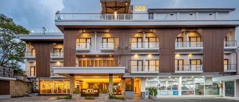 A multi-story hotel with a modern design, featuring balconies, a rooftop bar, and a well-lit entrance.