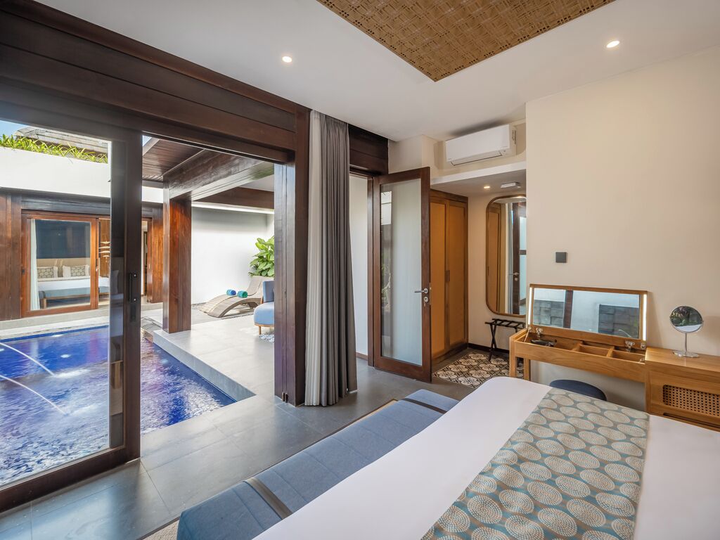 A modern hotel room with a large bed, a desk, a mirror, and a view of an outdoor swimming pool.