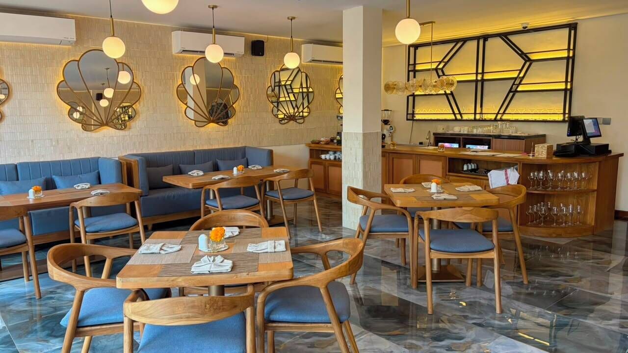 Un restaurante con mesas de madera y asientos acolchados azules, una zona de bar y apliques decorativos en las paredes.