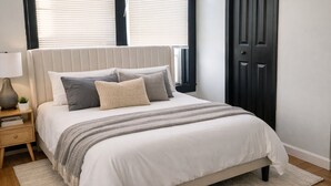 A bedroom with a bed, bedside table, lamp, and a dark door. - Fully Furnished One-Bedroom Near Downtown & Medical Center (Houston)