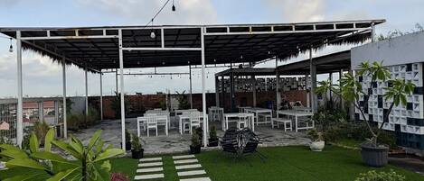 Un patio al aire libre con zona de estar cubierta, césped artificial y plantas en macetas.