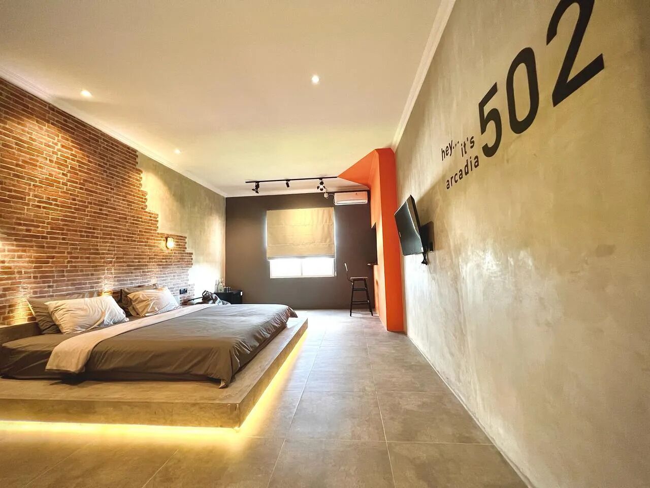 Un dormitorio moderno con una pared de ladrillo decorativa, una cama grande, un televisor y el número '502' en la pared.
