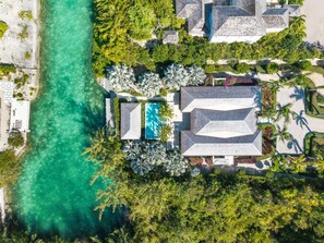 Luchtbeeld van een resort met een zwembad, omringd door weelderige begroeiing en een heldere turquoise zee.