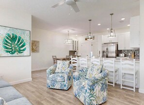 A modern kitchen with white cabinets, a stainless steel refrigerator, and a dining area with white chairs and a table. - Shared Heated Pool, Pickleball Court, Pet Friendly, Golf Cart Access (Port Aransas)