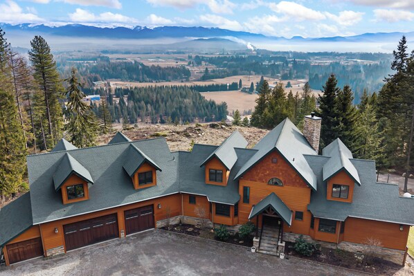 A large, multi-story house with a steeply pitched roof, multiple garage doors, and a stone chimney.