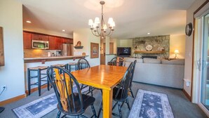 Un'area pranzo con tavolo e sedie in legno, un lampadario e una cucina sullo sfondo.