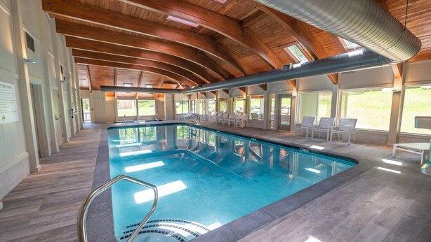 Una piscina interna moderna con soffitto in legno e pareti di vetro trasparenti.