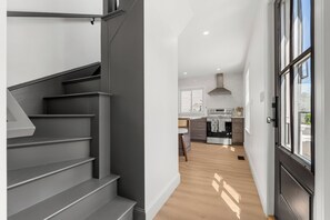 A modern kitchen with a built-in oven, a dining area with a table and chairs, and a staircase leading to another level. - The Coven House (Salem)