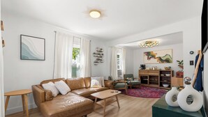 A modern living room with a leather sofa, a wooden coffee table, and a dining area with a wooden cabinet and chairs. - The Coven House (Salem)