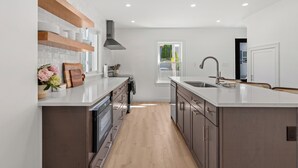 A modern kitchen with a central island, built-in appliances, and a window providing natural light. - The Coven House (Salem)