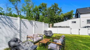 A backyard with a white fence, a house, and outdoor furniture including a cushioned chair and a table. - The Coven House (Salem)