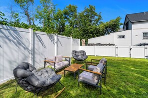 Ein Garten mit weißem Zaun, einem Haus und Gartenmöbeln, darunter ein gepolsterter Stuhl und ein Tisch.