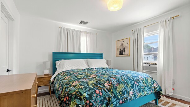 A bedroom with a teal bed, white curtains, a framed picture on the wall, and a view of the outside through a window. - The Coven House (Salem)