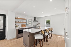 A modern kitchen with a central island, bar stools, and a built-in oven. - The Coven House (Salem)
