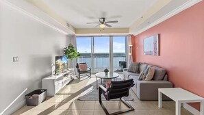 Uma sala de estar ampla com varanda, ventilador de teto e uma grande janela com vista para a cidade.