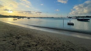 Ein Strand mit vor Anker liegenden Booten in ruhigem Wasser, einem wolkenlosen Himmel und einem Sonnenuntergang.