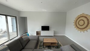 Ein modernes Wohnzimmer mit grauem Sofa, einem Holztisch und einem Flachbildfernseher auf einem weißen Schrank.