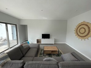 Ett modernt vardagsrum med en grå soffa, ett soffbord i trä och en platt-TV placerad på ett vitt skåp.
