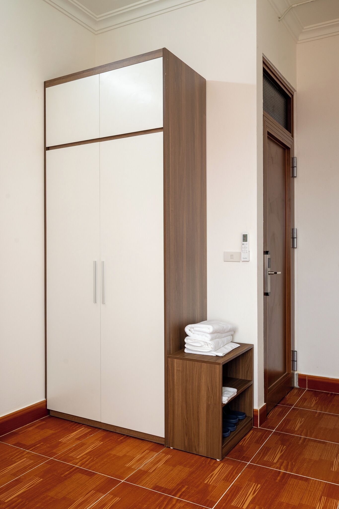A wardrobe with a wooden panel design, a shelf with folded towels, and a door with a handle.