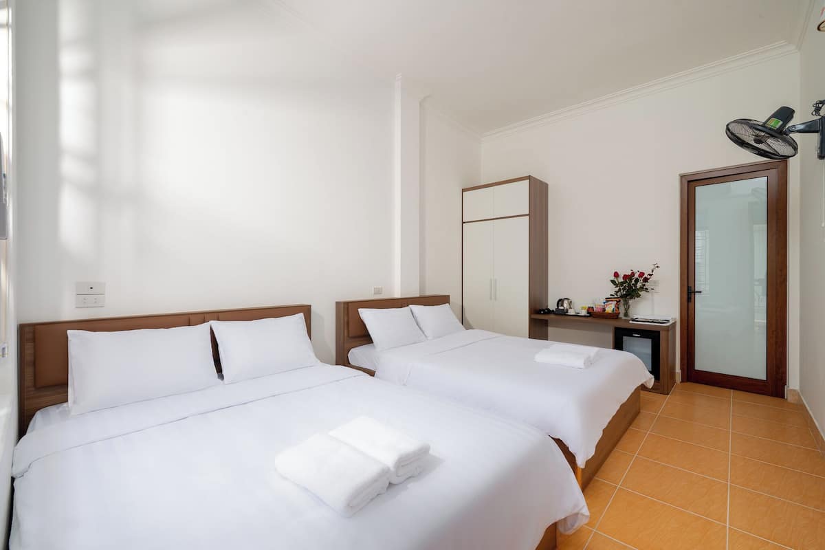 A hotel room with two beds, a small desk with a chair, a mirror, and a door with a glass panel.