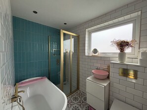 A bathroom with a bathtub, a shower, a sink with a vase of flowers, and a window. - Charming house with sauna in Glasgow perfect for your getaway (Glasgow)