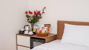 Ein Hotelzimmer mit einem Bett, einem Nachttisch mit Kaffeemaschine, einer Vase mit roten Rosen, einer Snackkörbchen und einer Wasserflasche.