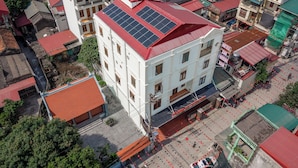 Ein mehrgeschossiges Gebäude mit Solaranlage auf dem Dach, umgeben von anderen Gebäuden mit roten Ziegeldächern.