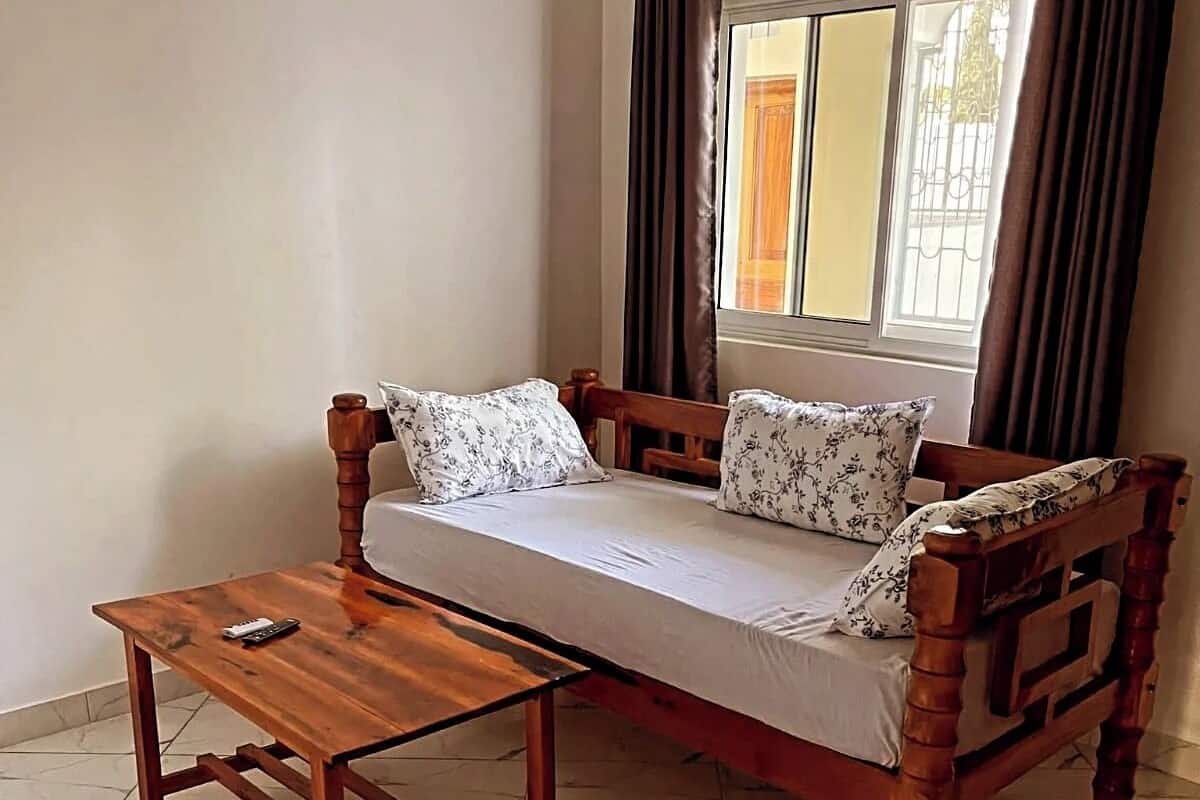 A wooden bed with a matching table, a window with curtains, and a tiled floor.