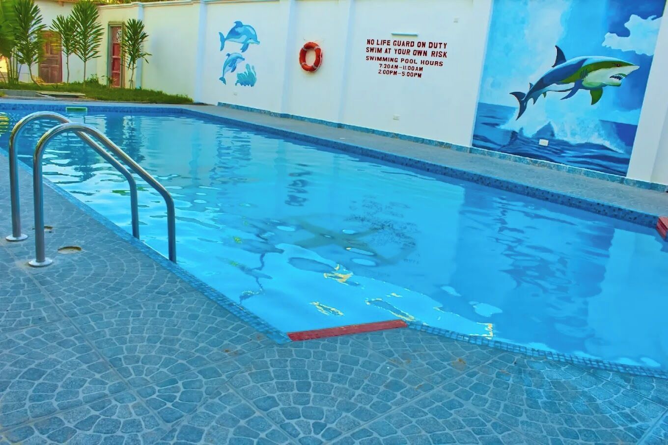 A swimming pool with a lifebuoy and a shark mural on the wall.