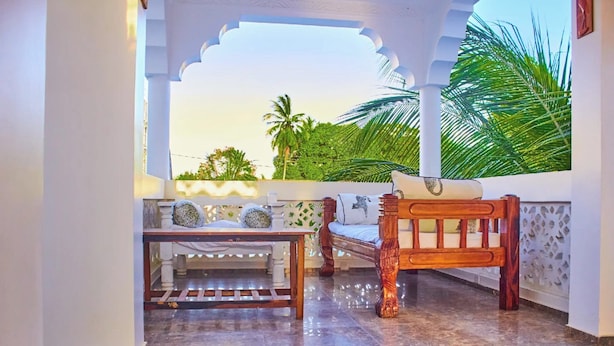 A covered outdoor seating area with a wooden bench and table, surrounded by white walls and a view of palm trees. - Milalana residence & Hotel Malindi (Malindi)