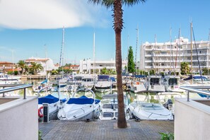 A marina with multiple boats docked, a palm tree, and a building with balconies in the background. - PORT CANIGO Duplex with private solarium (ROSES)