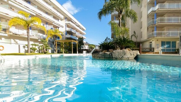 Una piscina con agua azul cristalina, rodeada de edificios de varios pisos con balcones y palmeras.