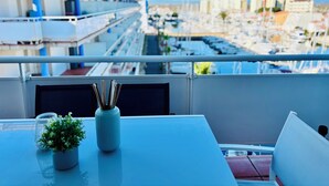 Un balcón con una mesa, una planta en maceta y vistas a un puerto deportivo y edificios.