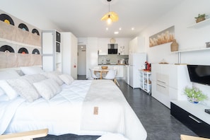 Ein modernes, helles Schlafzimmer mit einem großen Bett, einer kleinen Essecke und einer Küchenzeile.