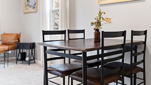 Un comedor con mesa de madera, sillas negras, un jarrón con flores y un cuadro en la pared.