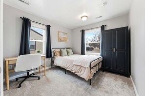 A bedroom with a bed, desk, chair, and wardrobe.